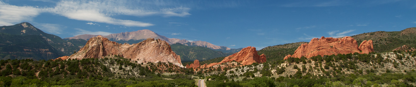 Beautiful image of the Garden of the Gods in Colorado Springs. Red rocks surrounded by lush mountain tops with green trees and blue skies.